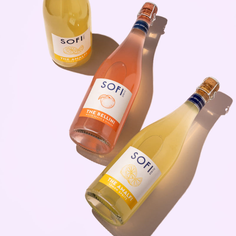 Three bottles of SOFI sparkling wine on a light purple background